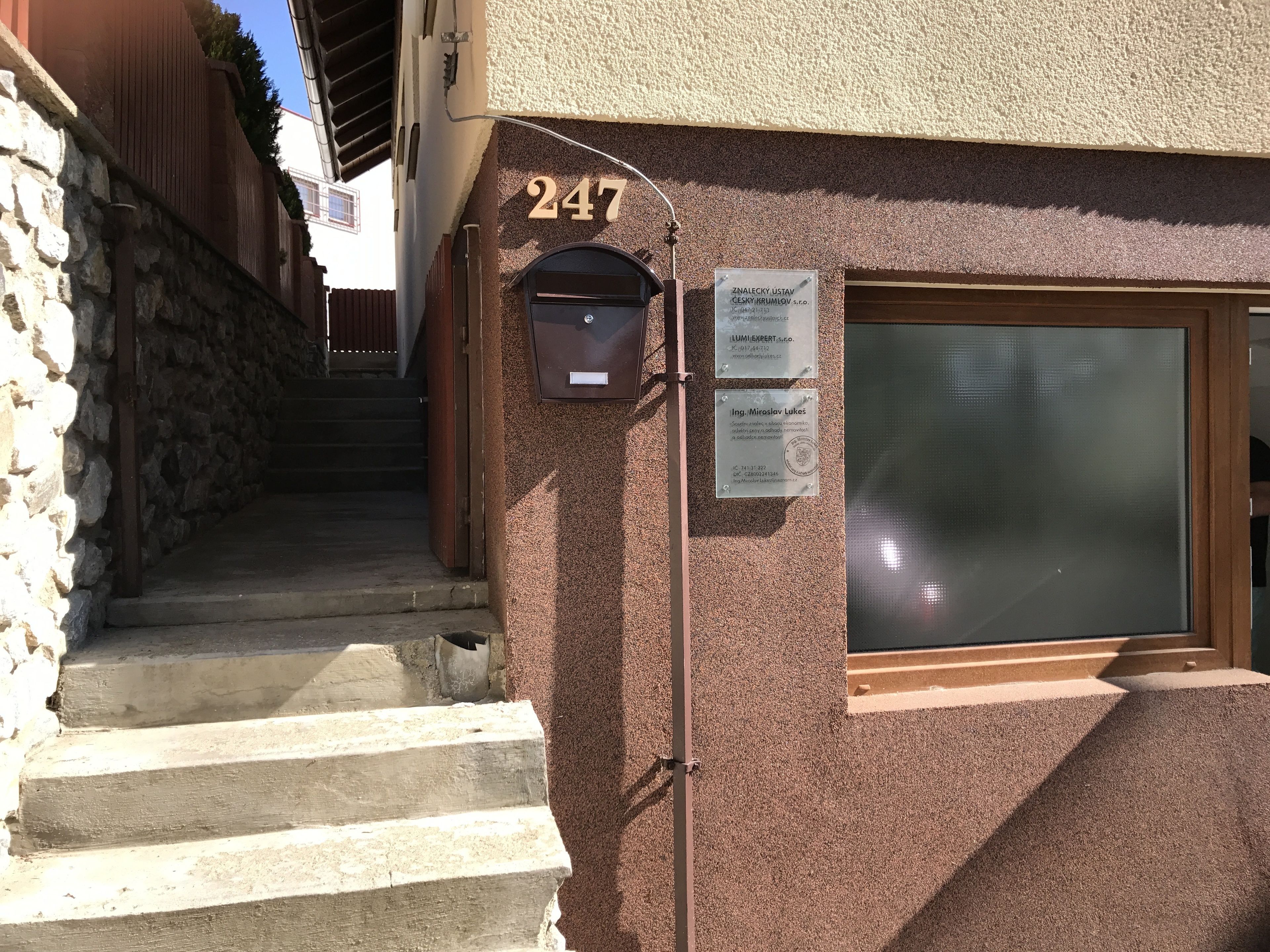 Um edifício com parede de pedra e escadaria de madeira que leva a uma porta com o número 247.