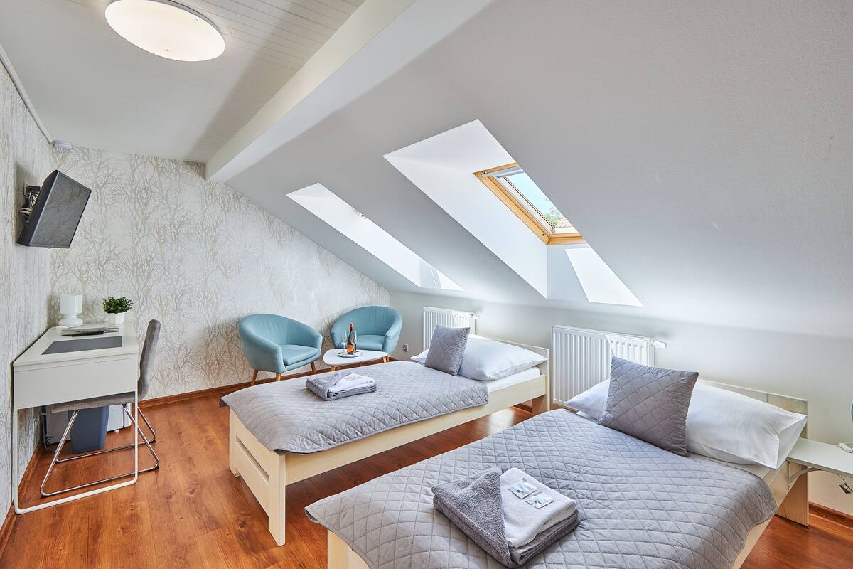 A modern loft bedroom with two beds, a desk, and a chair.