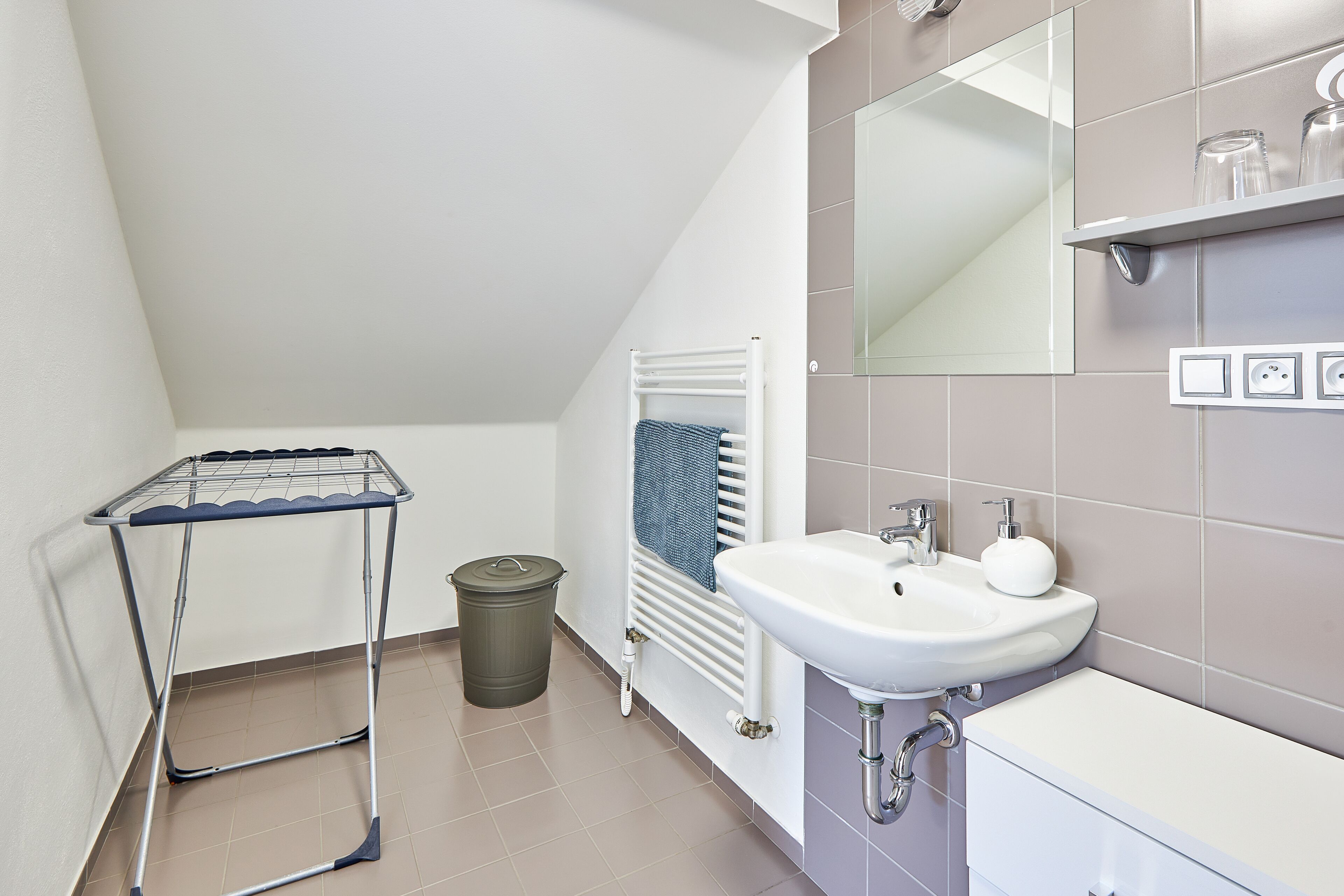 A modern bathroom with a white sink, a towel rack, a radiator, and a trash bin.