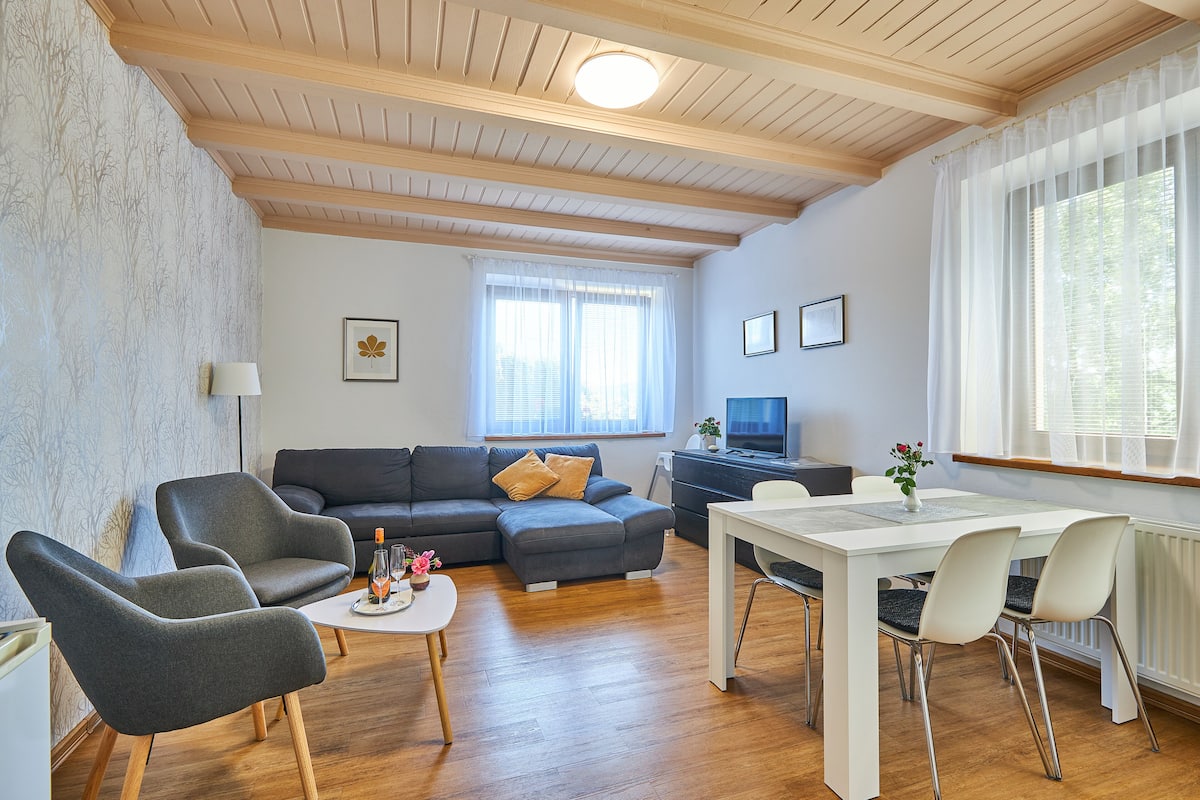 A modern living room with a sectional sofa, a dining table with chairs, and a TV.