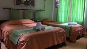 Habitación de hotel con dos camas, cada una con una colcha verde y una toalla blanca. Hay un cuadro en la pared, un teléfono y una mosquitera colgada junto a la ventana.