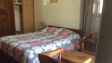 Quarto com cama, cadeira de madeira, mesa pequena, guarda-roupa e um quadro na parede.