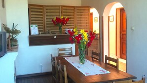 Un comedor con una mesa y sillas de madera, un jarrón con flores, y una cocina con armarios de madera y un ventanal.