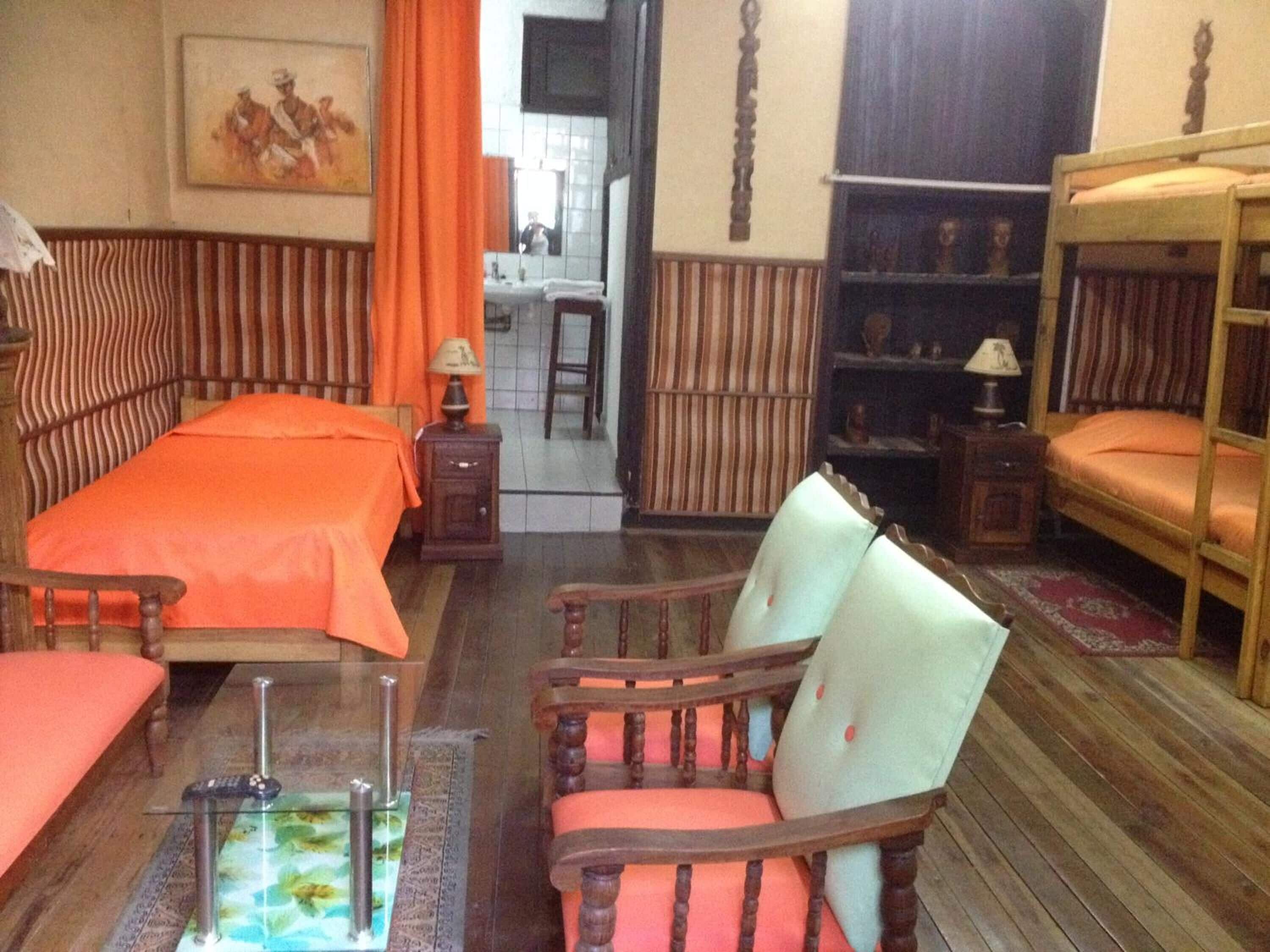 Una habitación con una cama, una silla, una mesita, una estantería y un espejo.