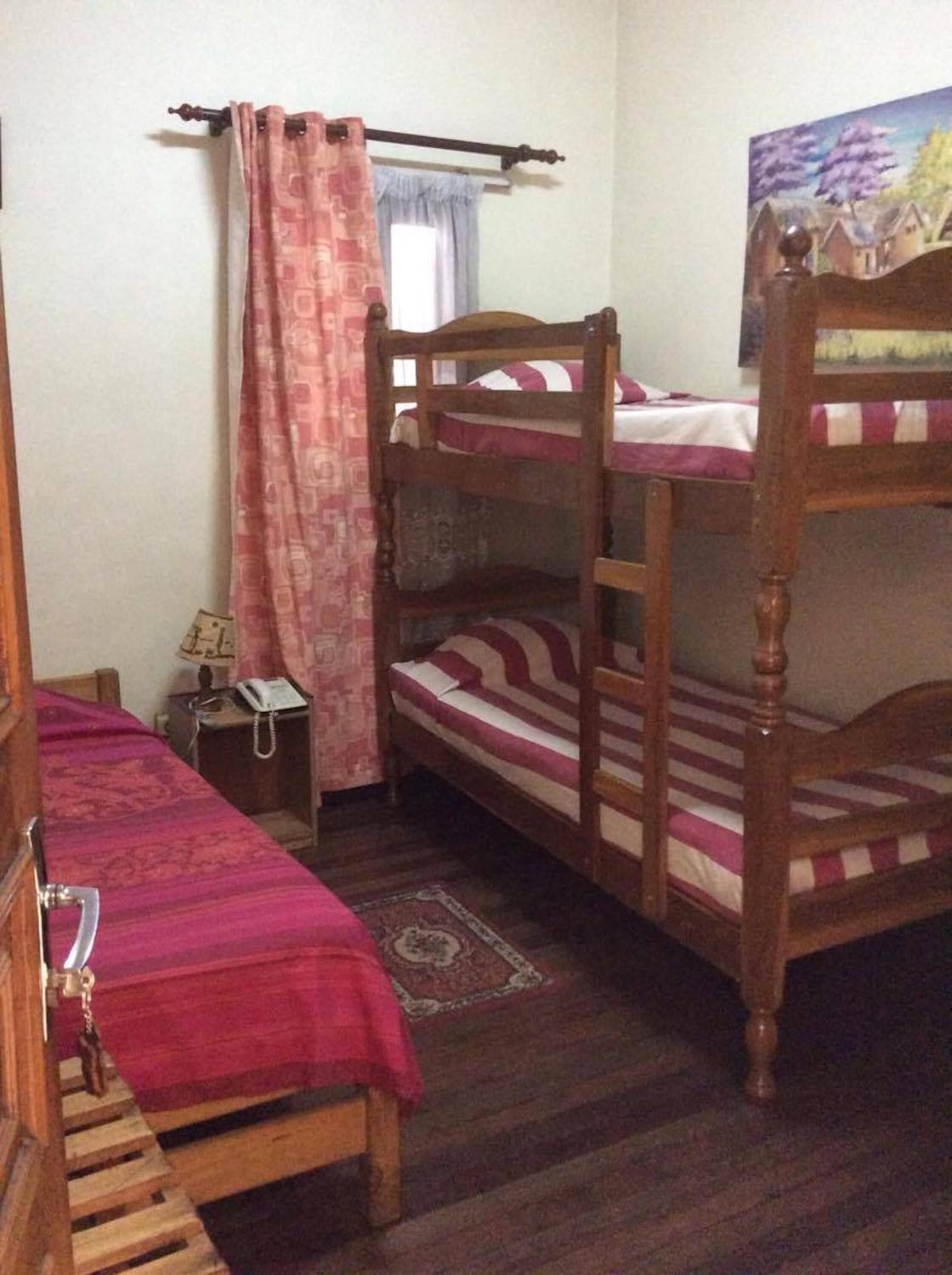 A room with two bunk beds, a small bedside table with a lamp, a patterned rug, and a painting on the wall.