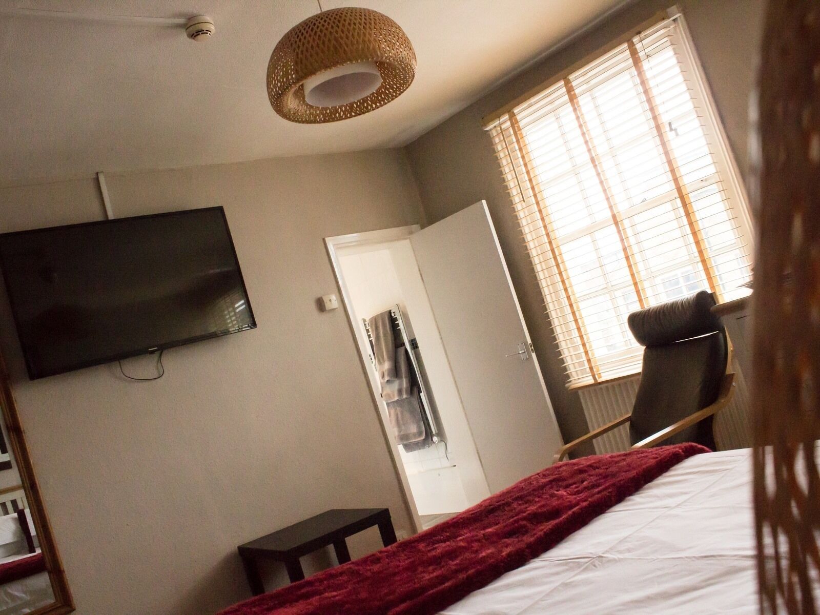 A bedroom with a bed, a TV mounted on the wall, a chair, a door, and a window with blinds.