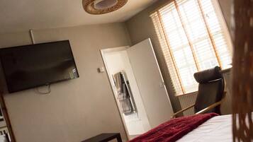 A bedroom with a bed, a TV mounted on the wall, a chair, a door, and a window with blinds.