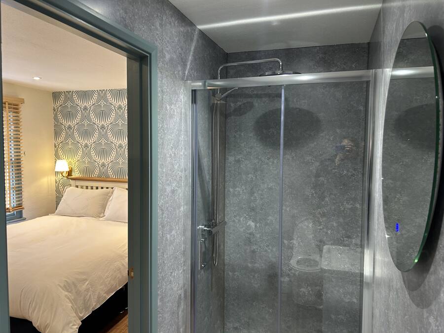 A modern bathroom with a glass shower enclosure, a large mirror, and a patterned wallpaper.