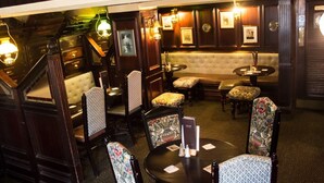 A cozy bar area with wooden furniture, patterned chairs, and wall-mounted lamps. - The Ship (Chelmsford)