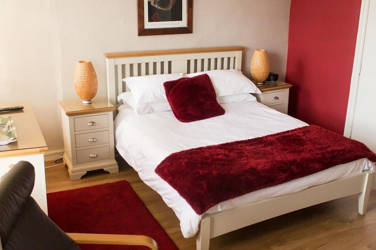 A neatly arranged bedroom with a bed, bedside tables, a chair, and a red rug.