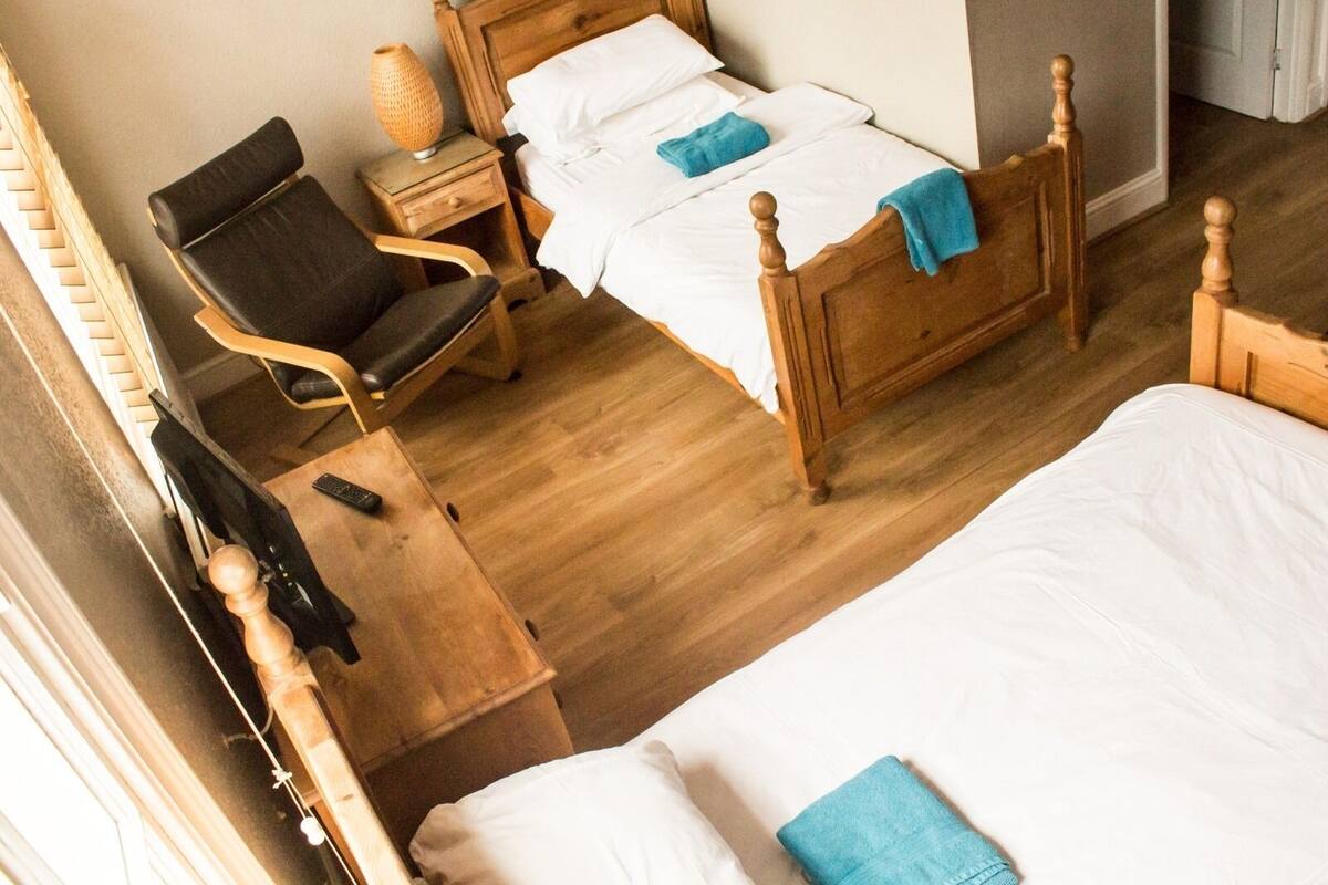 A room with two wooden beds, a chair, a bedside table, and a lamp.