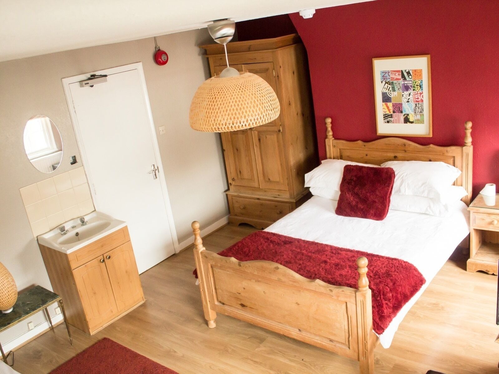 A bedroom with a wooden bed, a bedside table, a nightstand, a mirror, a wardrobe, and a hanging lamp.
