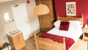 A bedroom with a wooden bed, a bedside table, a nightstand, a mirror, a wardrobe, and a hanging lamp.