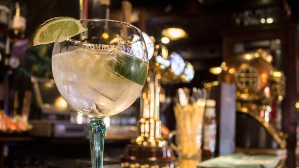 A bar setting with a glass of a clear, possibly alcoholic beverage garnished with a lime slice, on a bar counter with a green cloth underneath. - The Ship (Chelmsford)