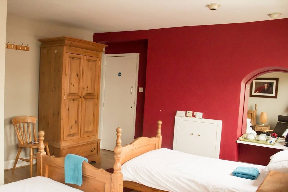 A room with two wooden beds, a wooden wardrobe, a chair, a desk with a tray, and a mirror.