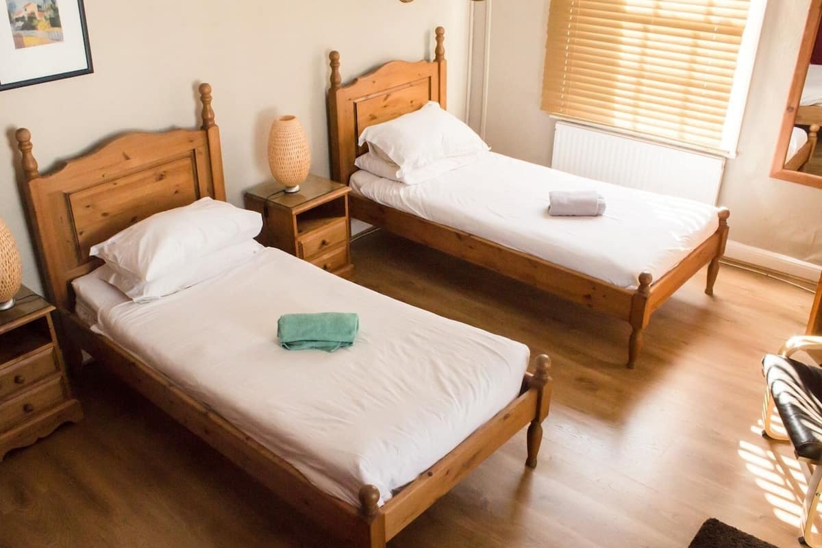 A room with two wooden beds, nightstands, a lamp, and a window with blinds.