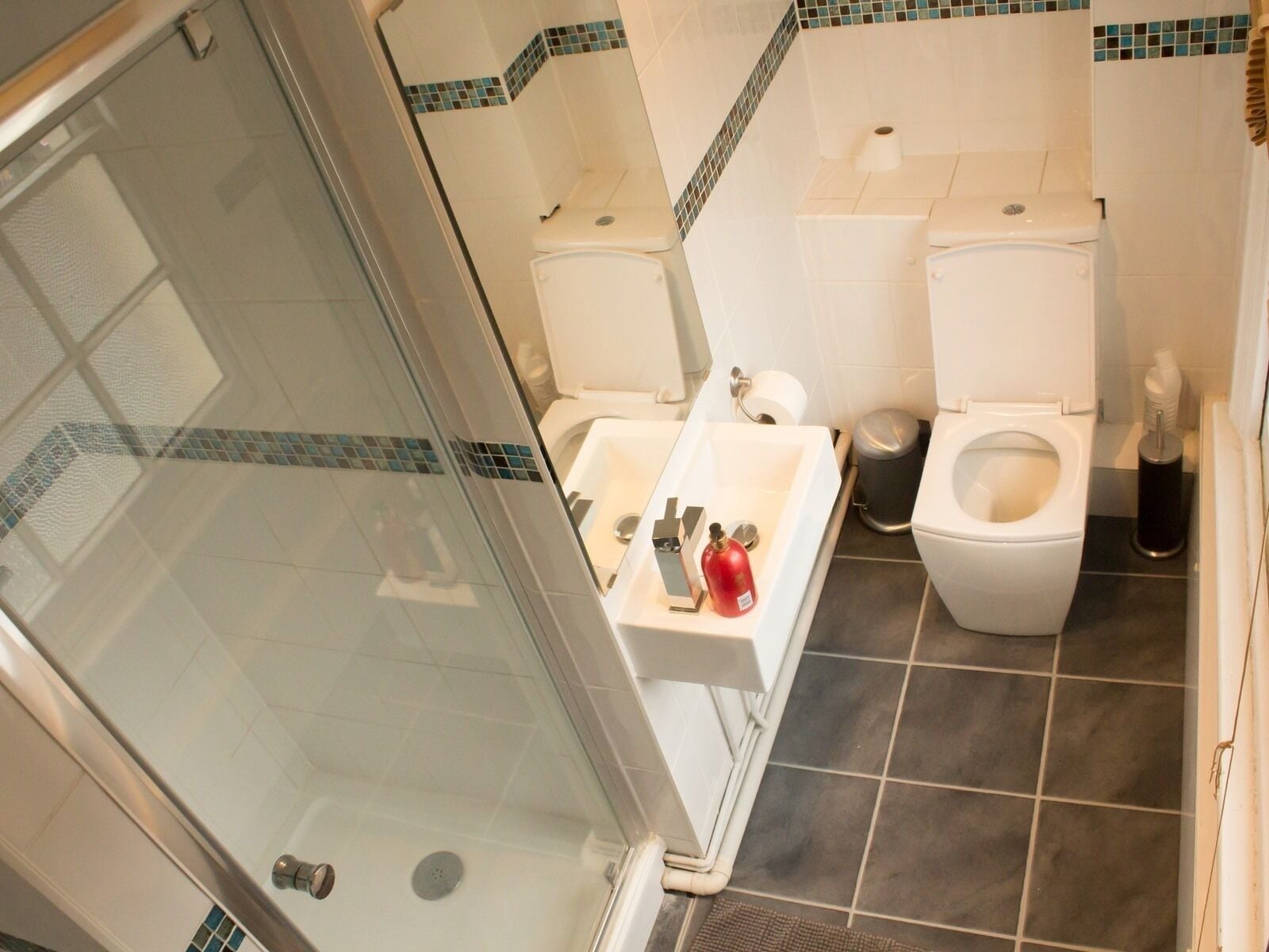 A bathroom with a glass shower enclosure, a sink with a mirror, and two toilets.