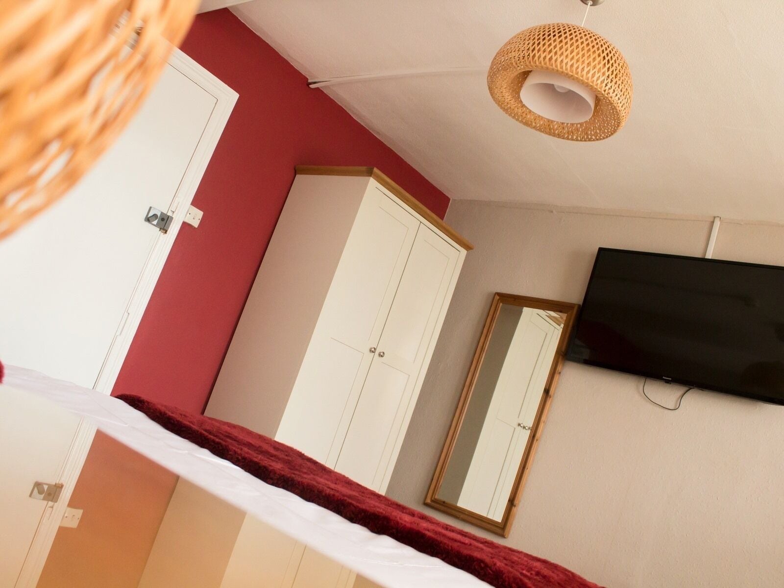 A bedroom with a bed, a wardrobe, a mirror, and a television on the wall.