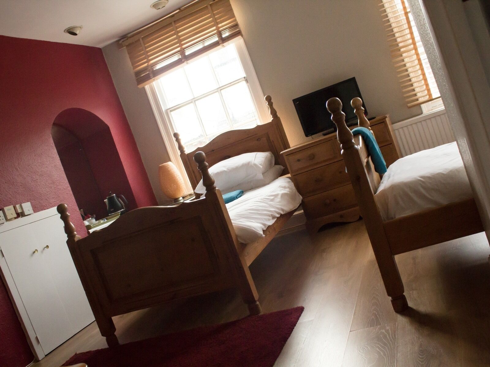 A bedroom with a wooden bed, a bedside table, a TV, and a window with blinds.