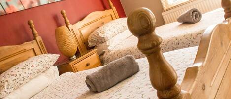 A hotel room with two wooden beds, floral bedding, a bedside lamp, and a window with blinds.