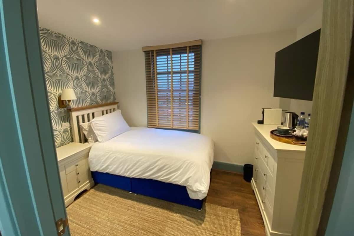 A bedroom with a bed, nightstand, dresser, and a window with blinds.
