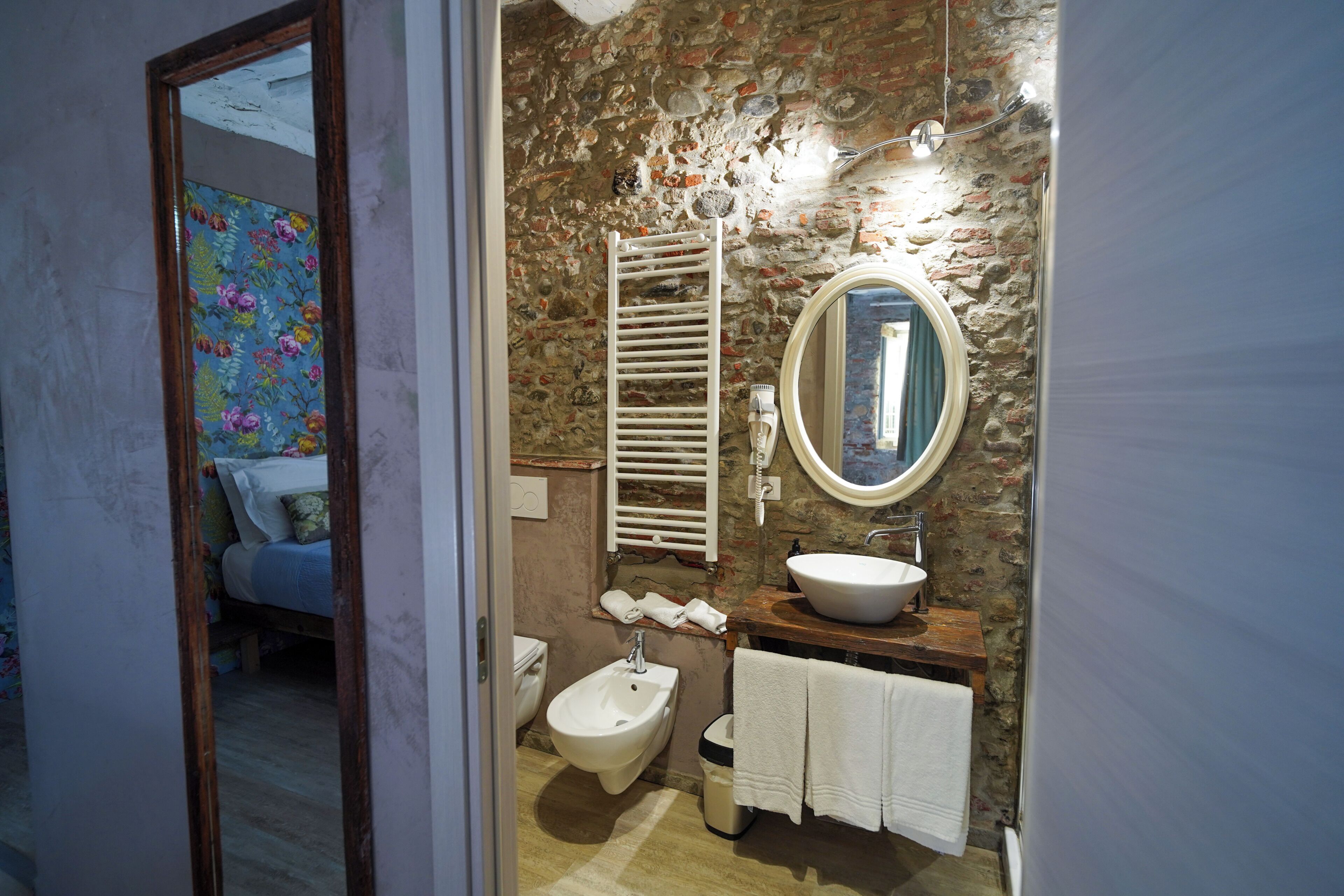 Een badkamer met een stenen muur, een hygiëneschuimer, een wastafel, een spiegel en een handdoekhouder.
