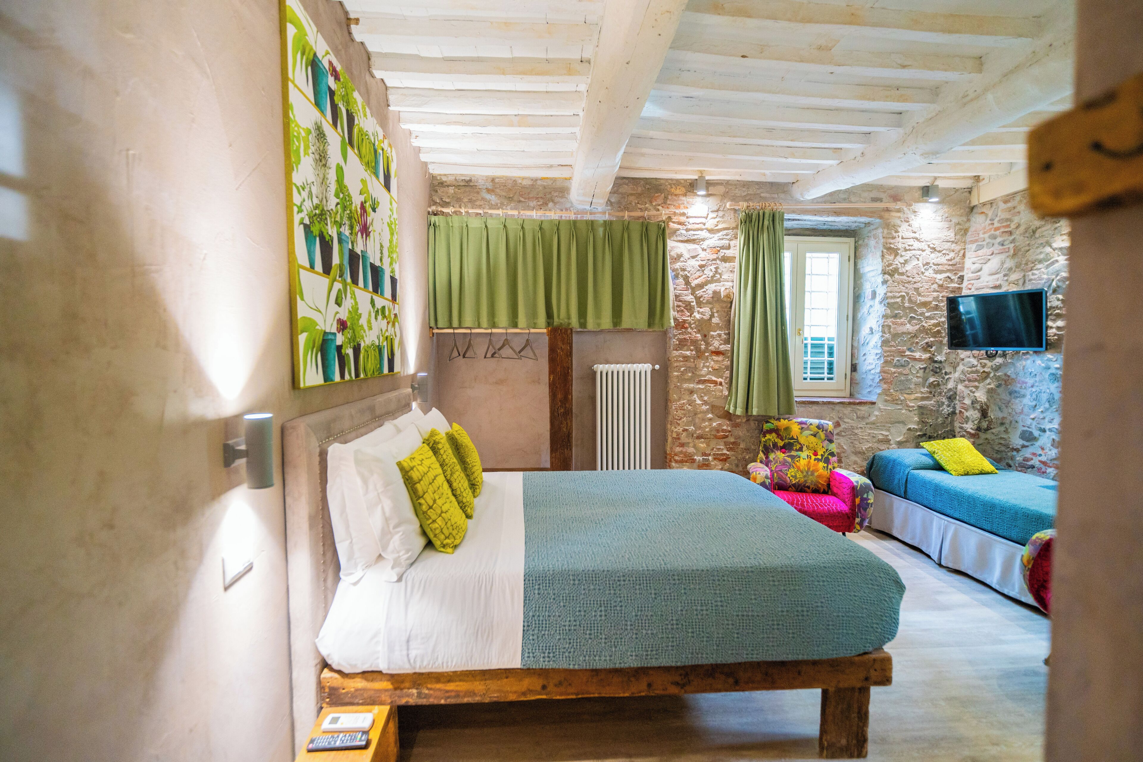 A bedroom with a bed, a wall-mounted TV, a stone wall, and a window with curtains.