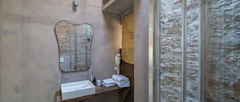 A bathroom with a sink, mirror, towel rack, and shower area.
