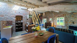 Un interior rústico con pared de piedra, muebles de madera, una escalera y vistas al exterior.