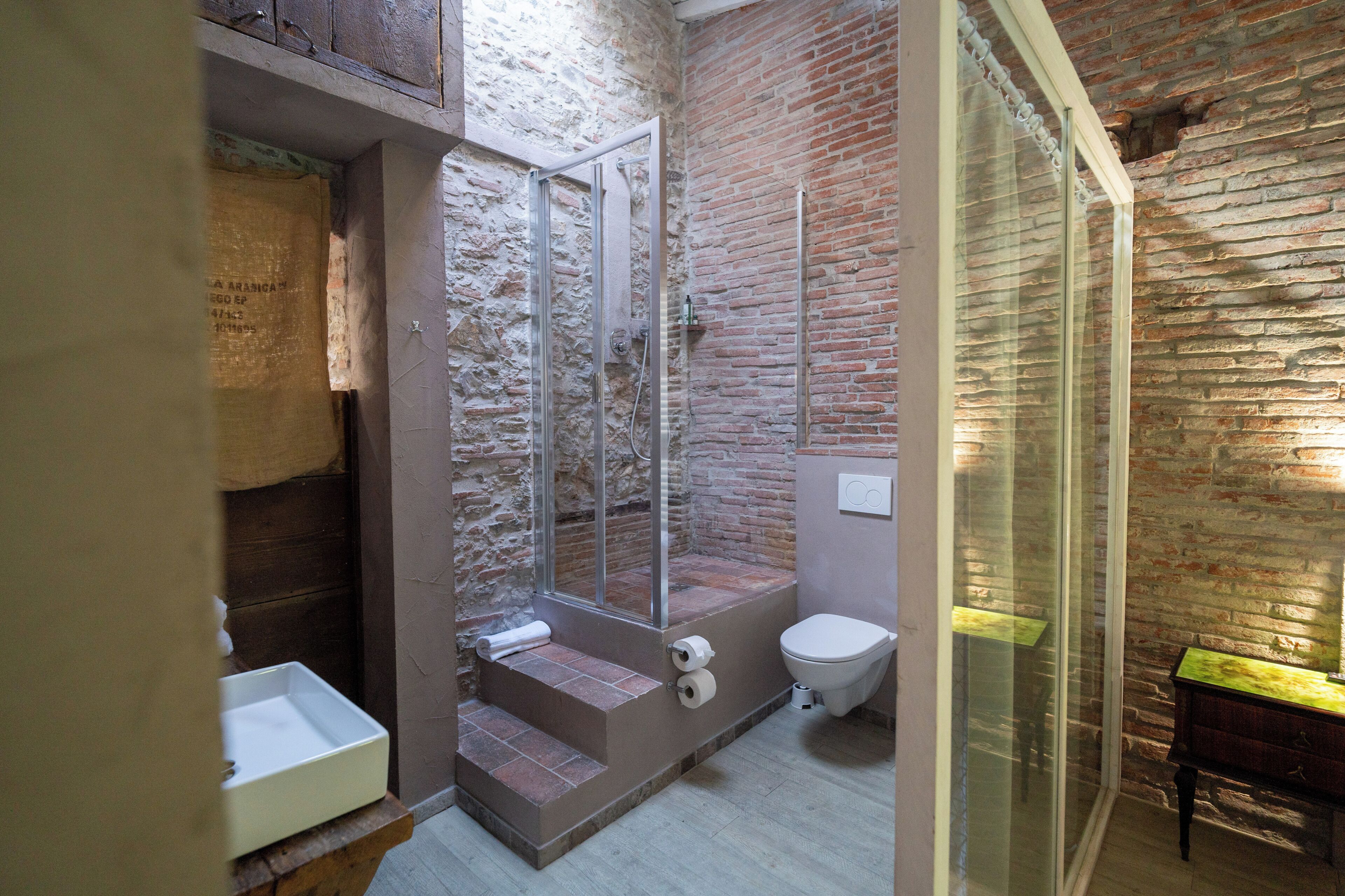 Ein Badezimmer mit Dusche, Toilette und Waschbecken, das Ziegelwände und eine Glasdusche aufweist.