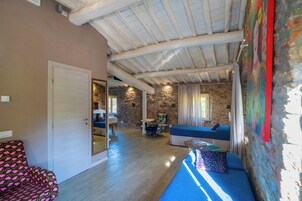 Una stanza con parete in pietra, soffitto in legno, un divano, una poltrona e un letto.