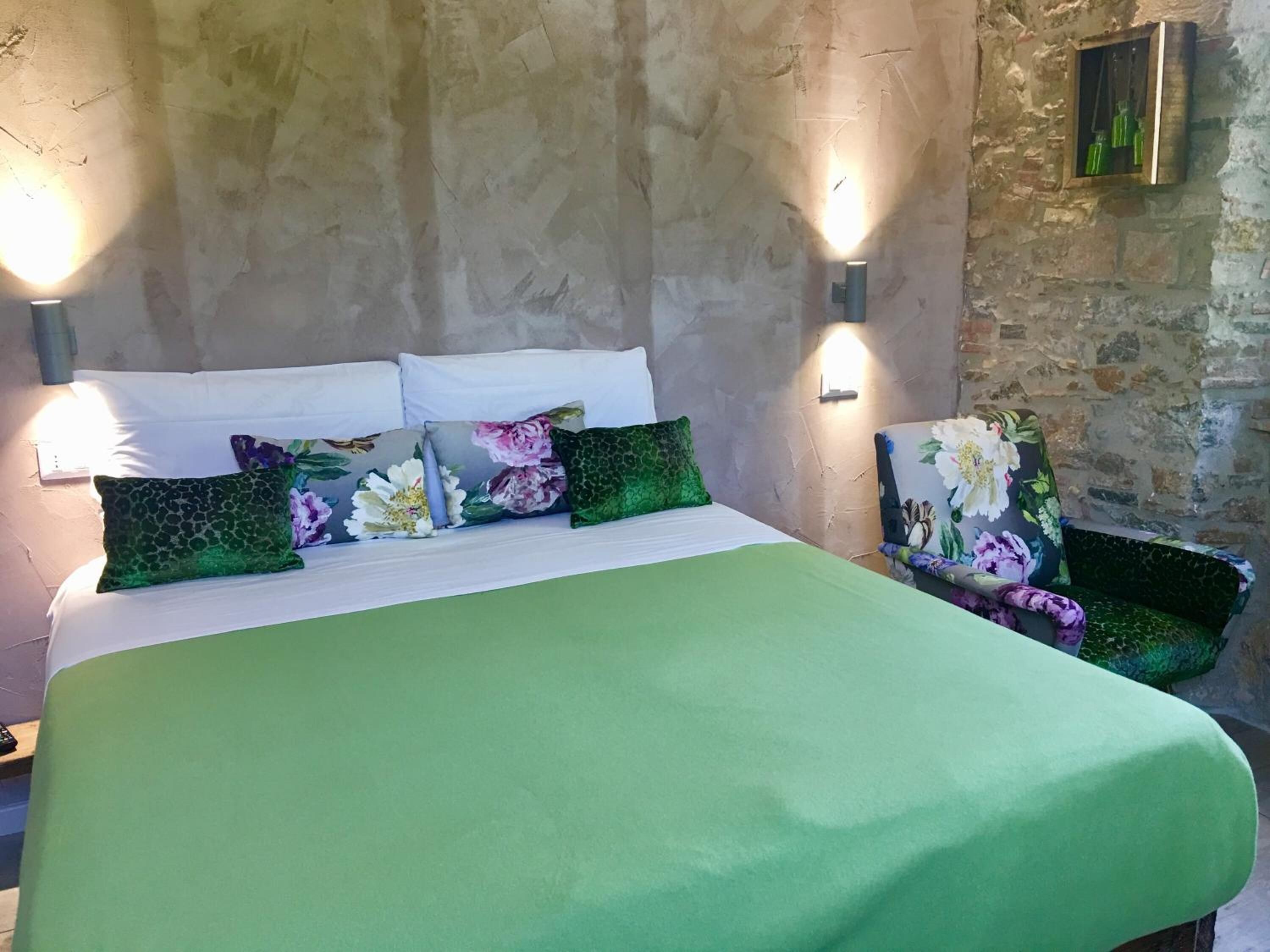 Una cama con colcha verde, varios almohadones y dos luces fijadas a la pared.