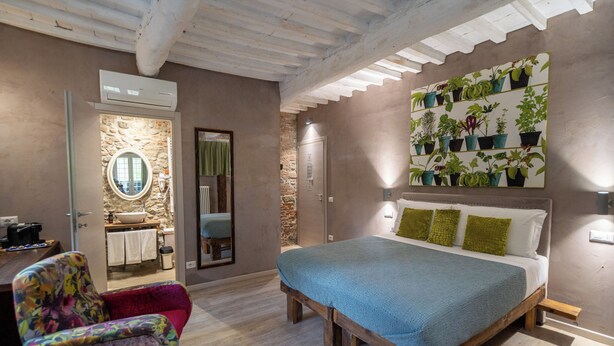 Un dormitorio con cama, una silla, un estante para plantas en la pared, y un baño visible a través de una puerta abierta.