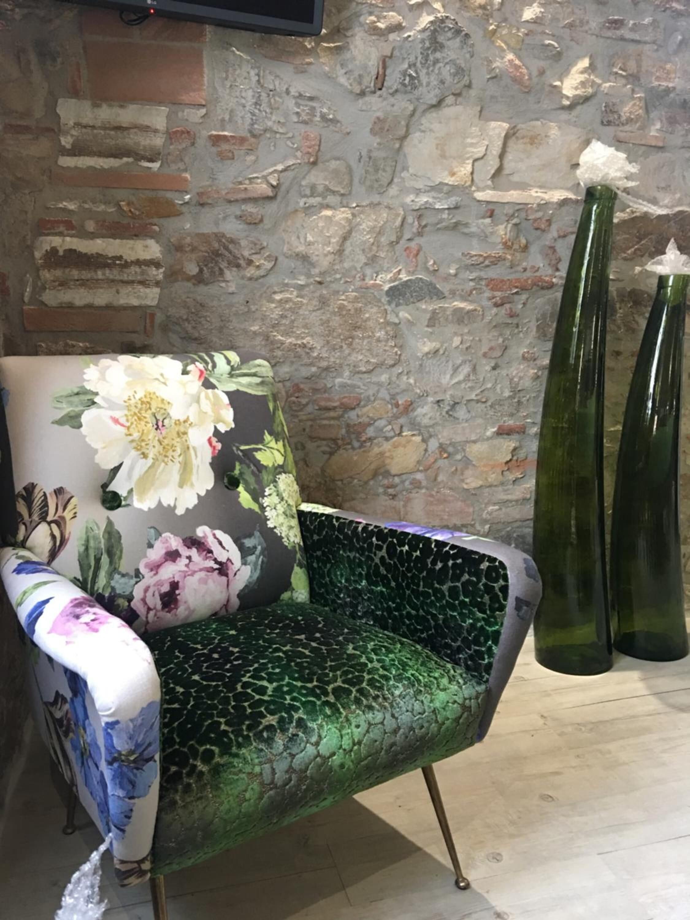 Una silla con un cojín floral y un asiento verde texturizado, ubicada frente a una pared de piedra con dos jarrones verdes.