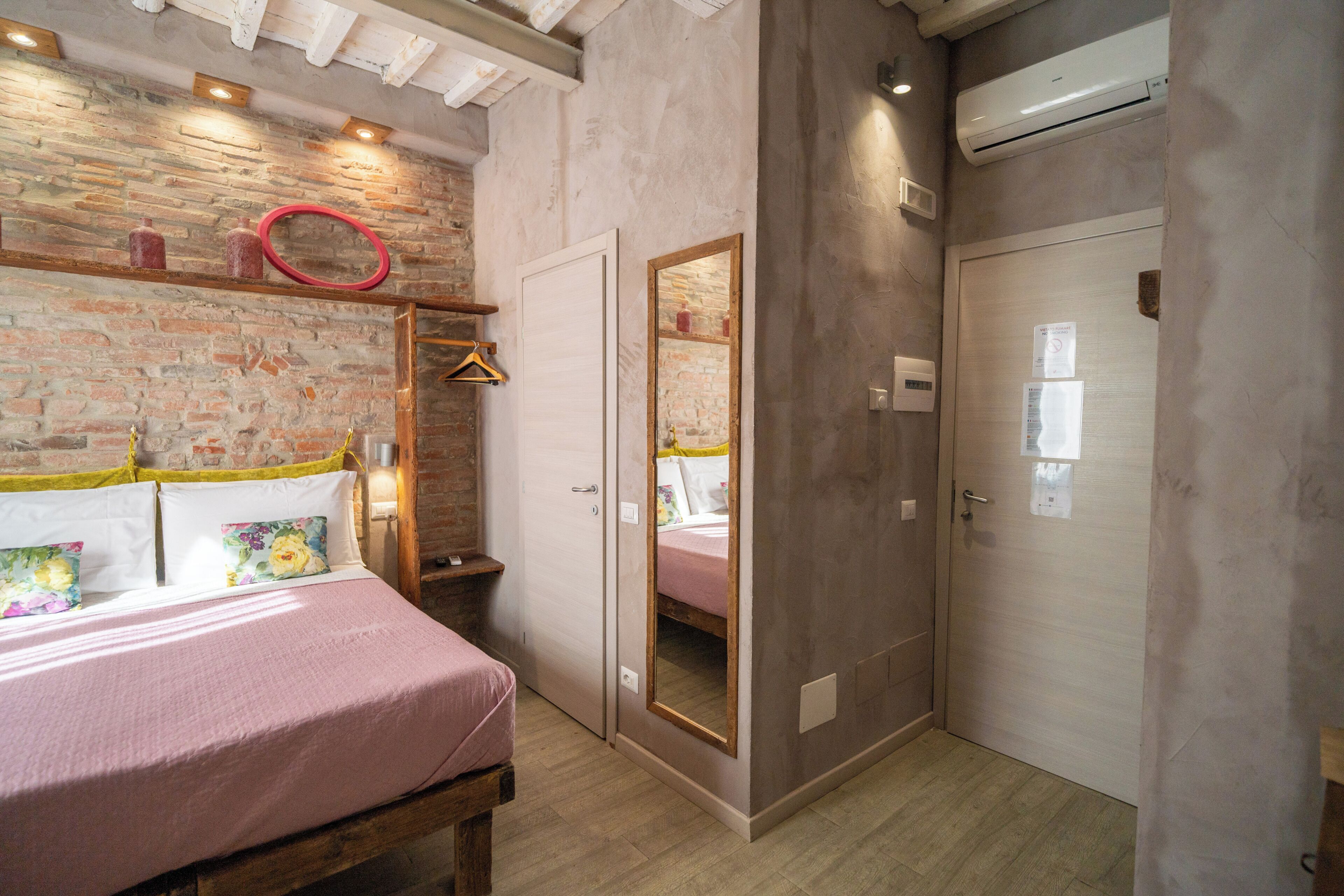 A bedroom with a bed, a mirror, a wardrobe, and a brick wall.