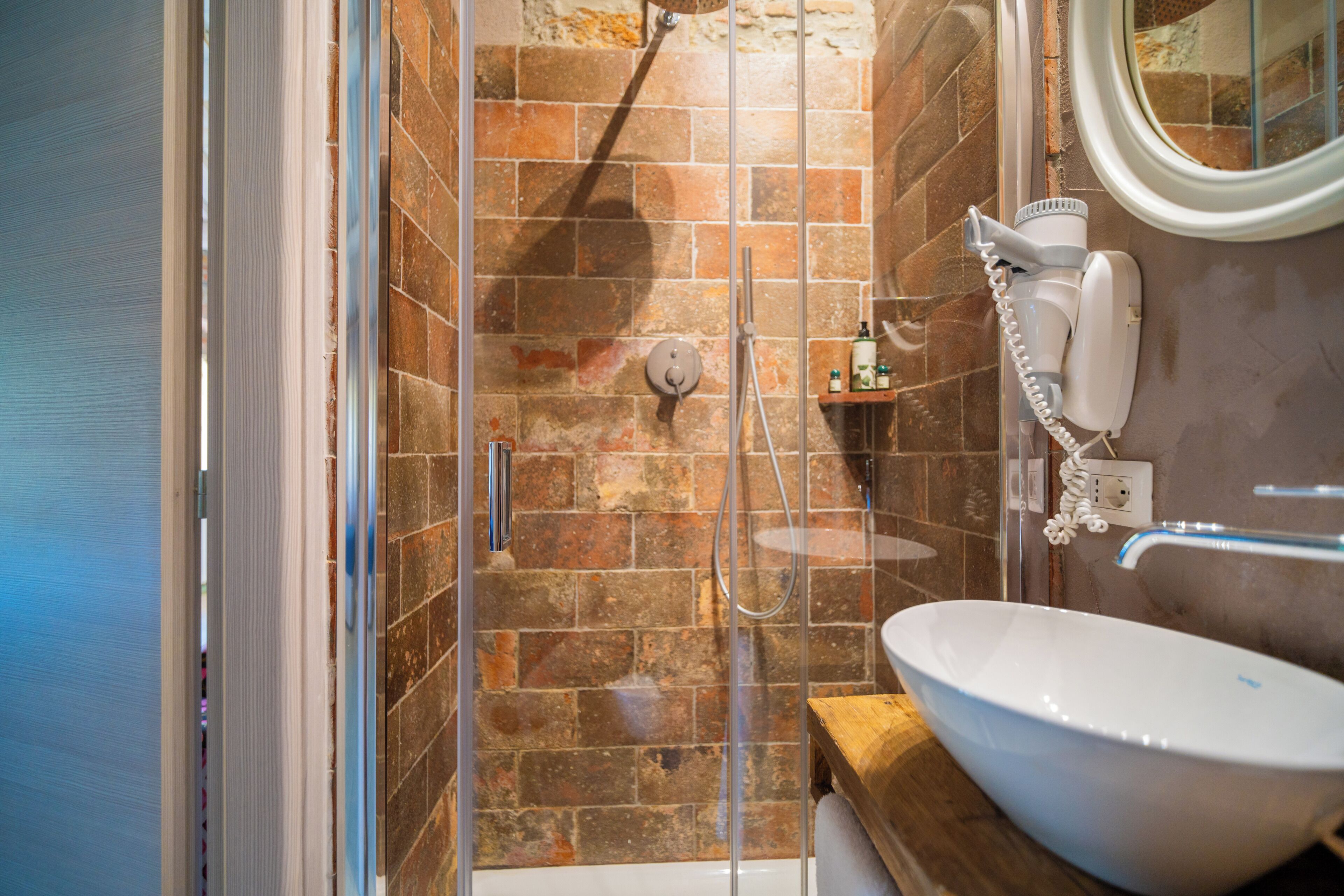 A bathroom with a glass-enclosed shower, a white sink, and a hairdryer on a shelf.