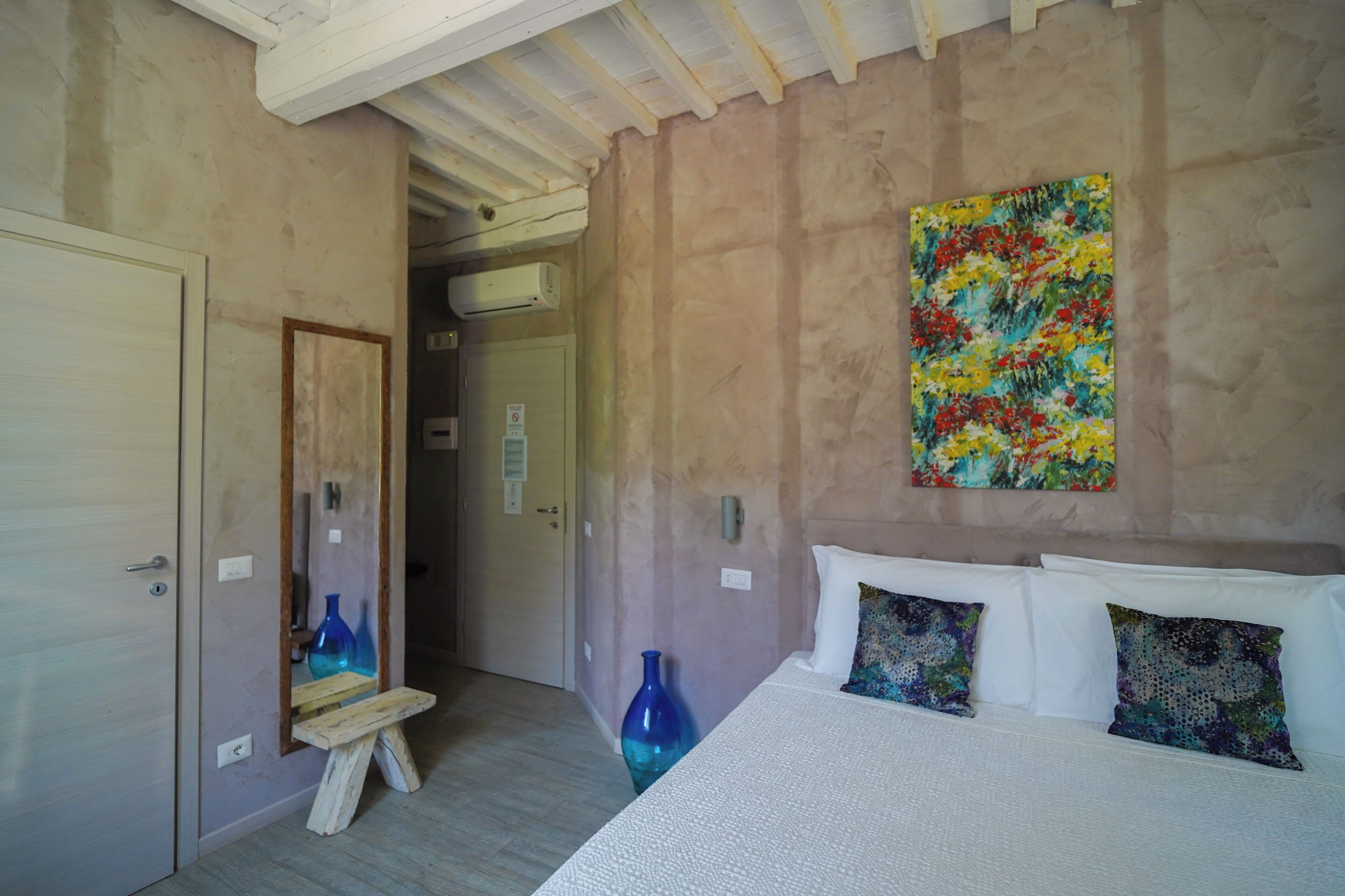 Une chambre à coucher avec un lit, des oreillers, un tableau, un miroir et un banc en bois.