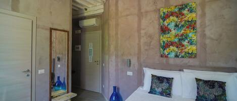 A bedroom with a bed, pillows, a painting, a mirror, and a wooden bench.