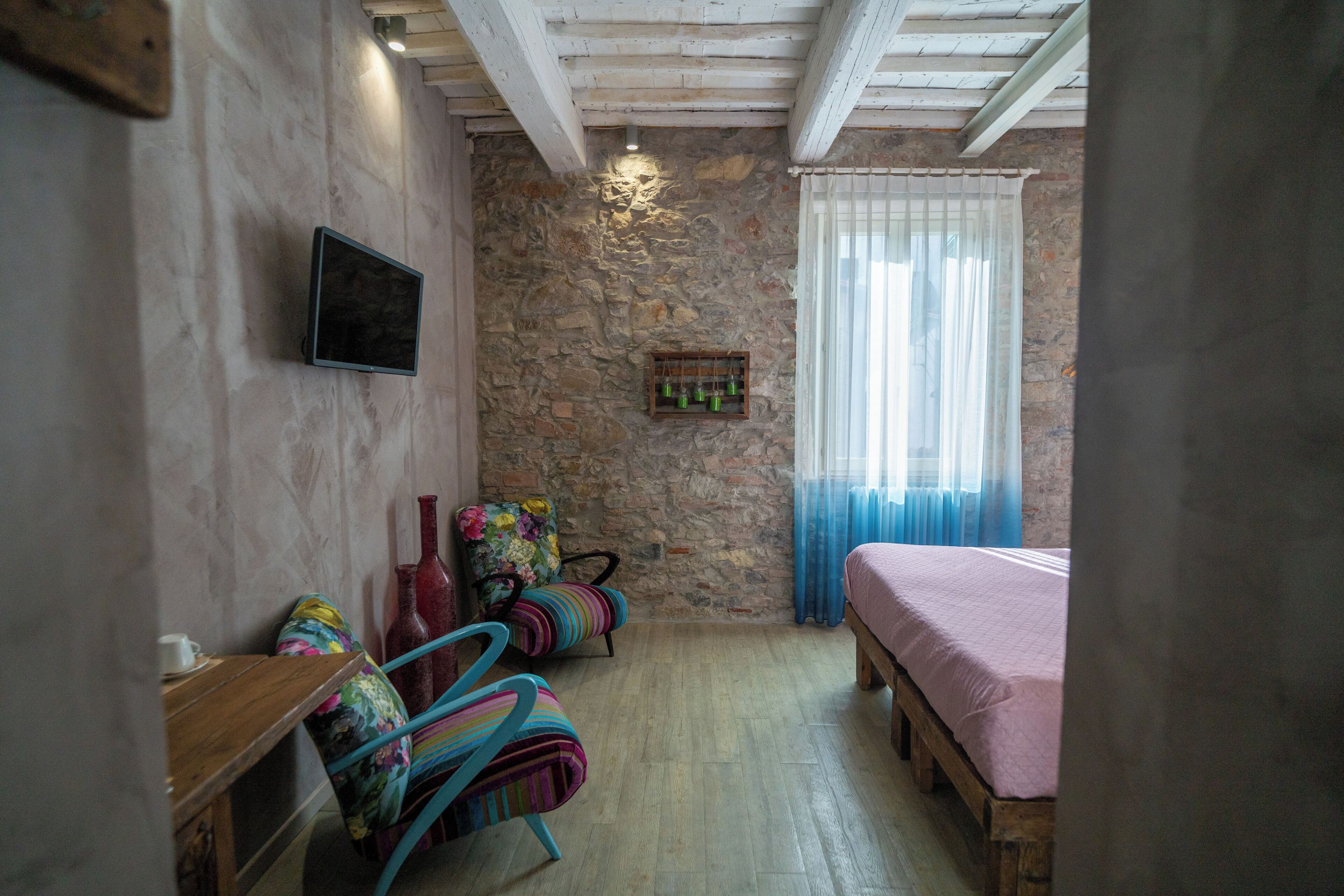 A bedroom with a stone wall, a bed, a wooden bench, a chair, and a television.