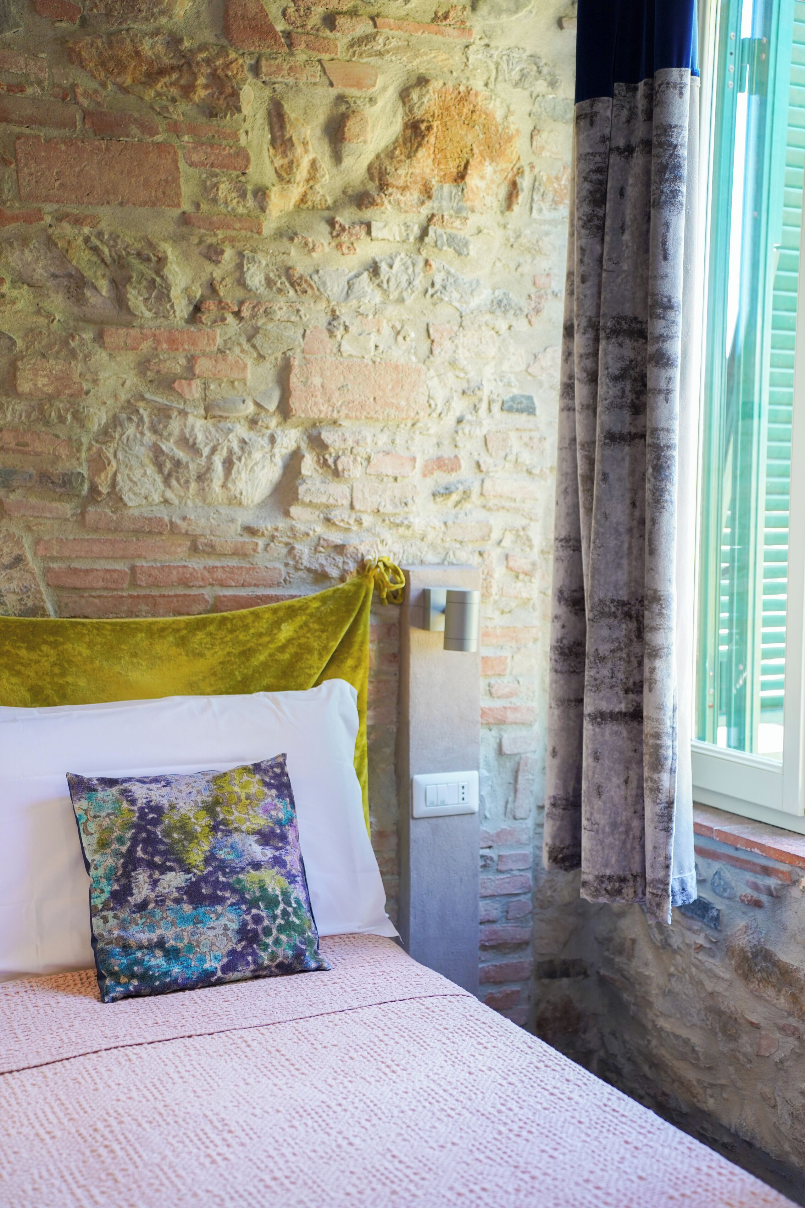A room with a brick wall, a bed with a green headboard, a white pillow, and a colorful pillow.