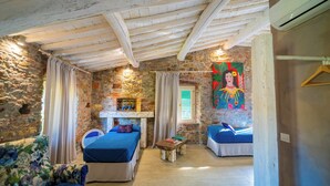 Una habitación rústica con vigas de madera a la vista, paredes de piedra, una cama, un sofá y un mural colorido.