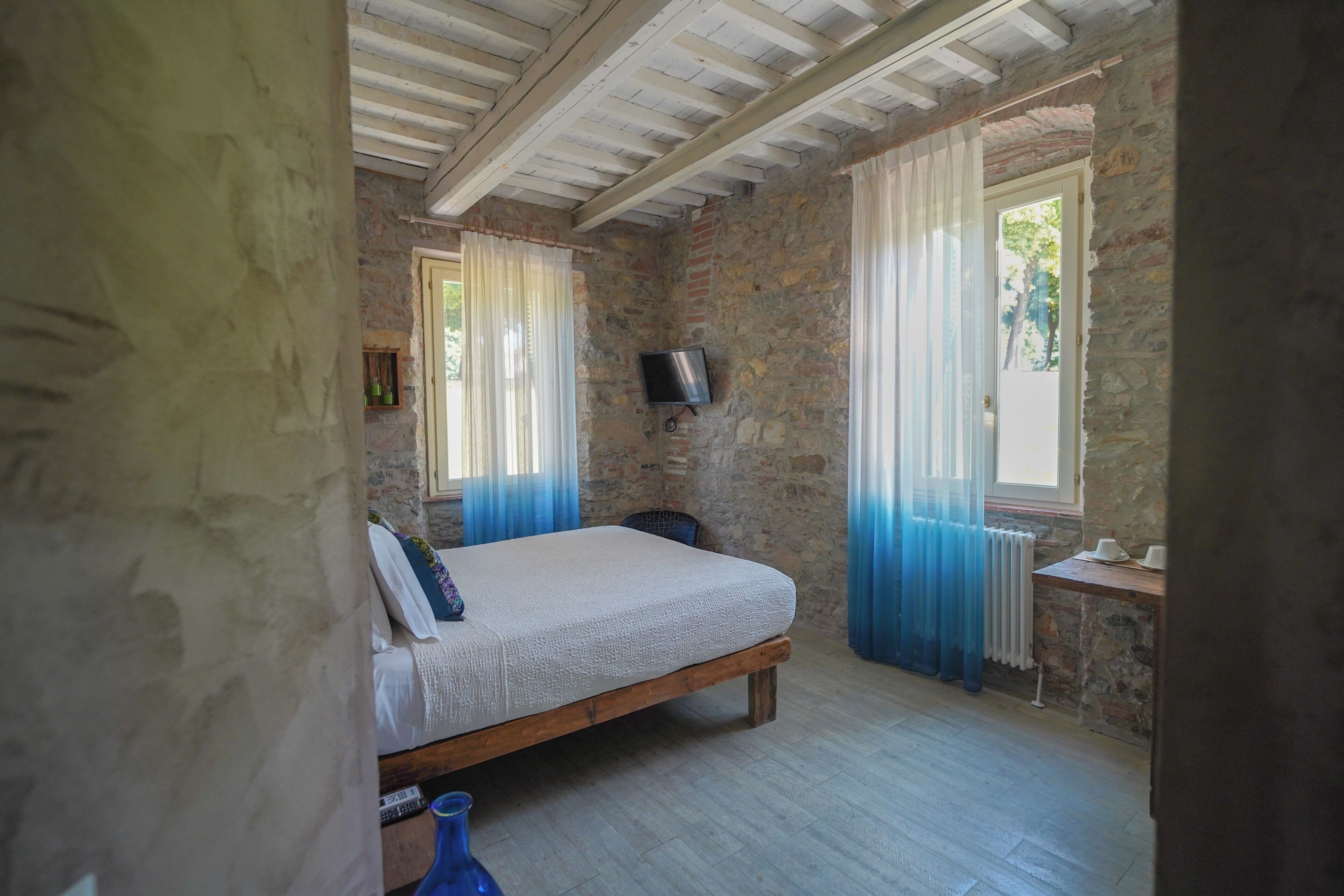 A bedroom with a wooden bed, stone walls, a television, and a window with curtains.