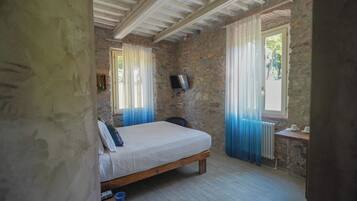 A bedroom with a wooden bed, stone walls, a television, and a window with curtains.