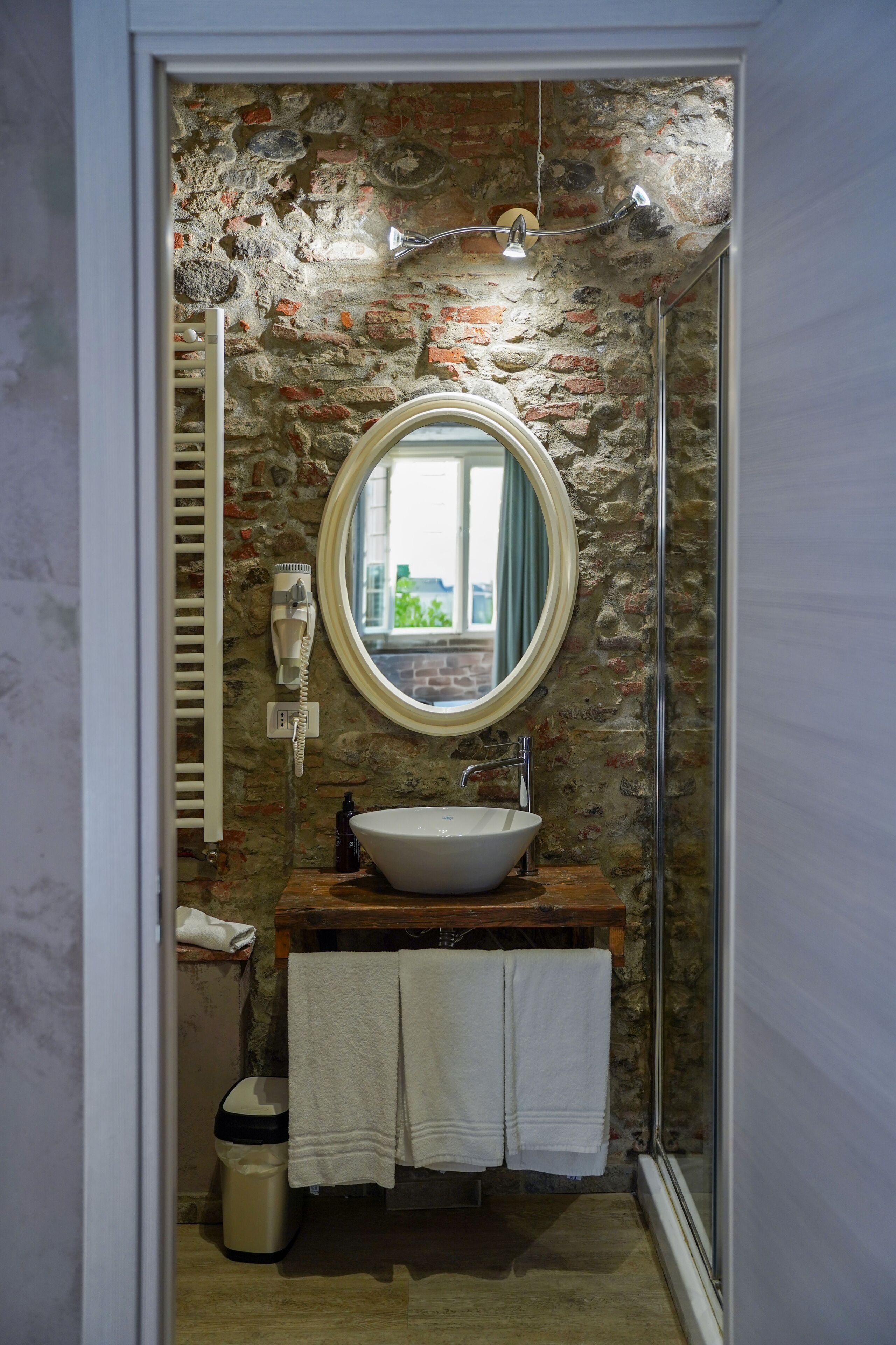 Un baño con pared de piedra, espejo redondo, lavabo y ducha.
