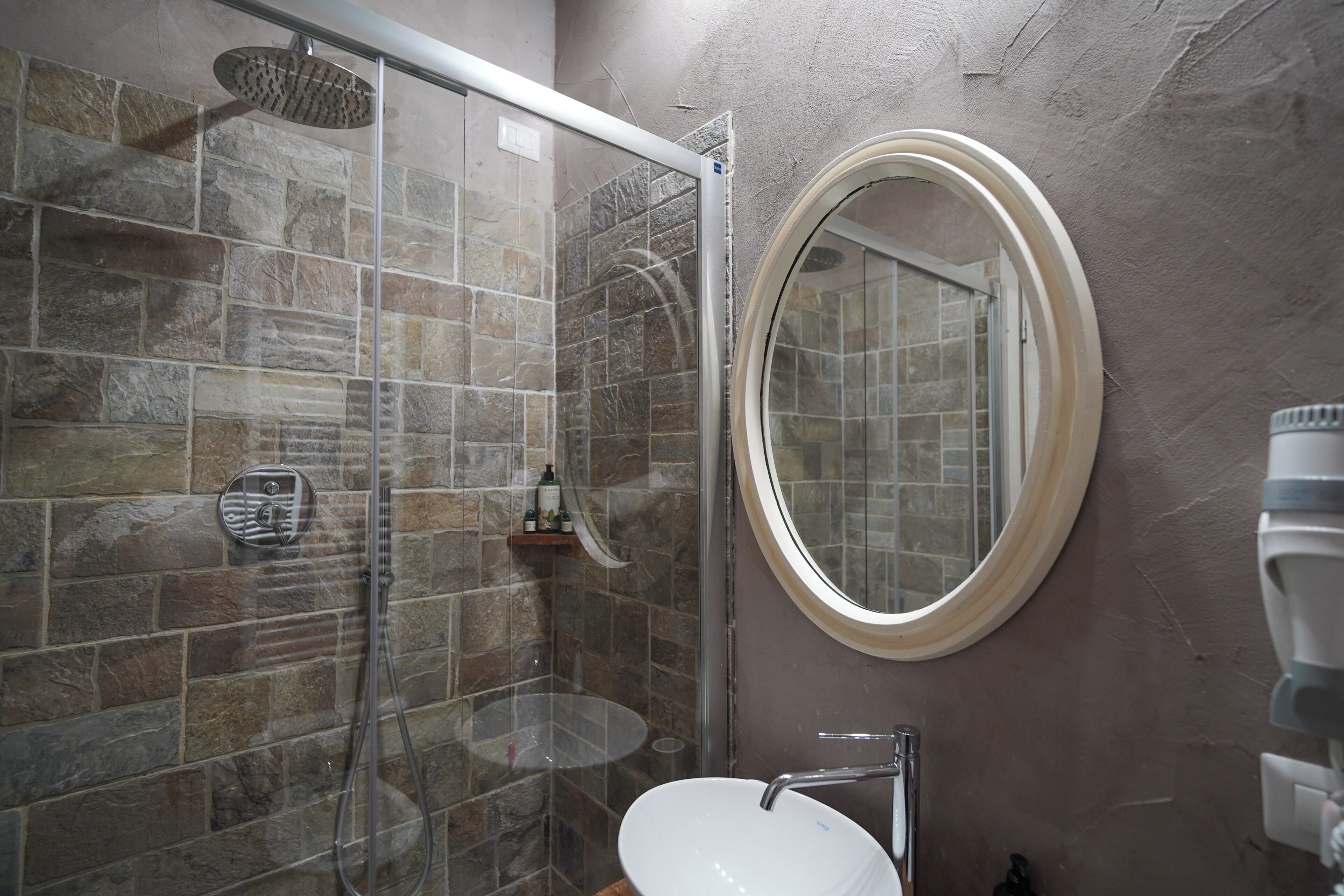 Un baño con ducha de vidrio, espejo redondo y lavamanos blanco.