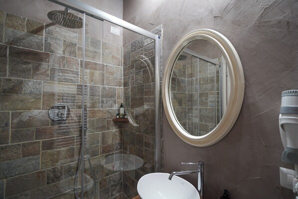 A bathroom with a glass-enclosed shower, a round mirror, and a white sink. - Inside the Wall (Lucca)