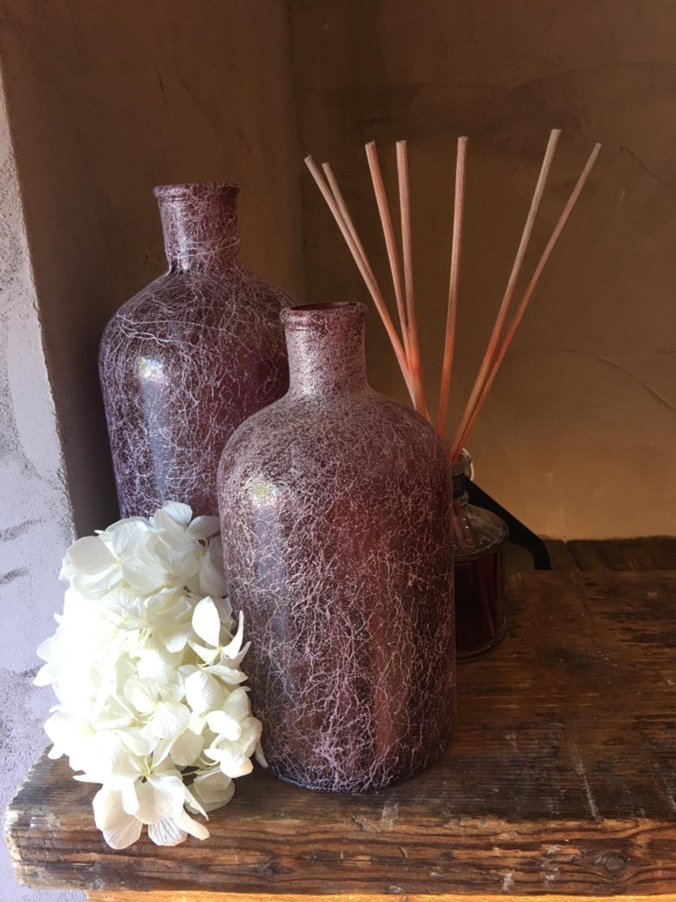Dos jarrones con textura y un ramillete de flores blancas sobre una superficie de madera.