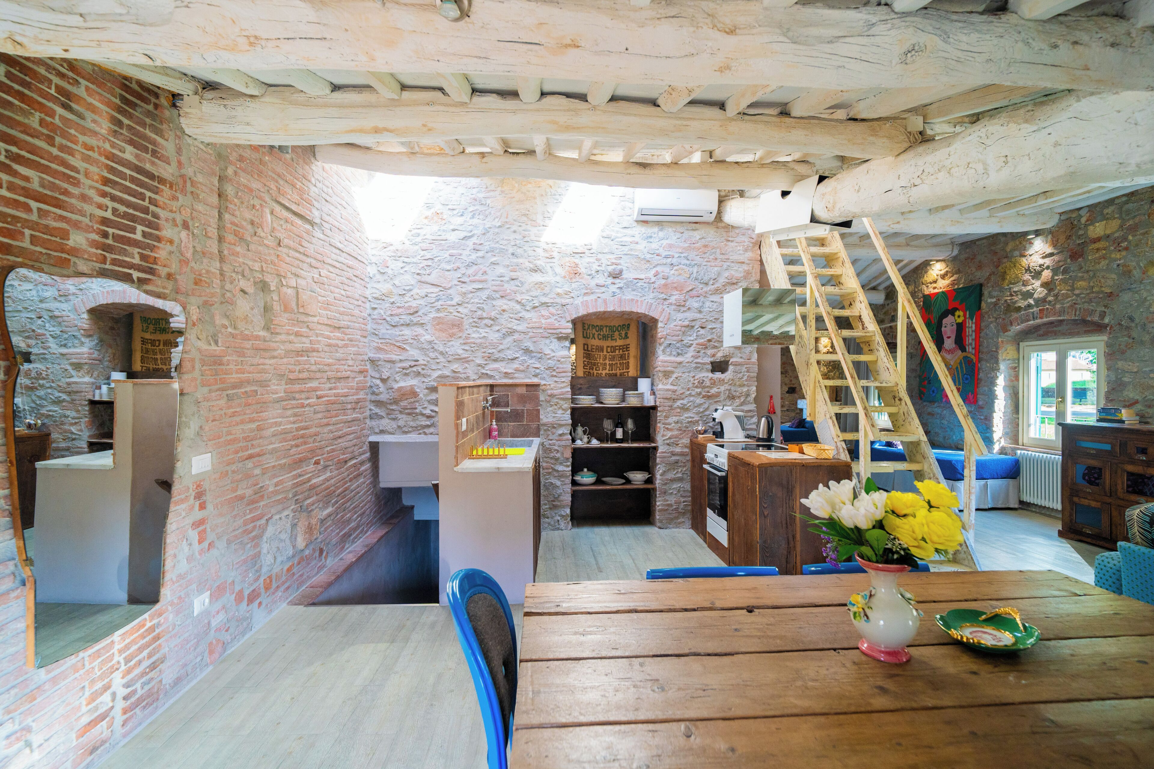 A rustic interior with exposed brick walls, a wooden table, a vase with flowers, and a ladder leading to a loft area.