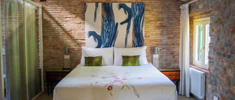 A bedroom with a brick wall, a large bed with white bedding, two green pillows, and a floral design.
