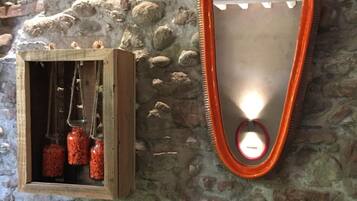 Un mur de pierres rustiques surmonté d’une boîte en bois contenant des bocaux en verre suspendus et d’un miroir avec un cadre orange.